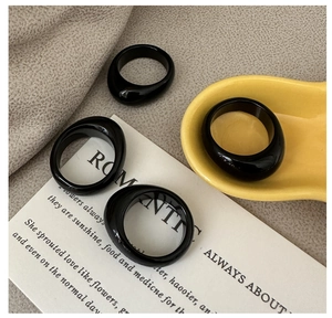 Close-up of four glossy black resin chunky rings on a decorative yellow ceramic tray