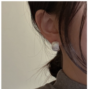 Detail of matte silver C-shape stud earring with cubic zirconia on model's ear