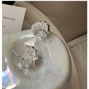 Gros plan de boucles d'oreilles créoles C en argent 925 avec texture ondulée plissée
