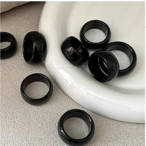Detailed view of wide black resin rings with a glossy finish on white ceramic display