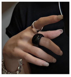 Close-up of minimalist silver thick ring and black glossy curved ring with a woven bracelet