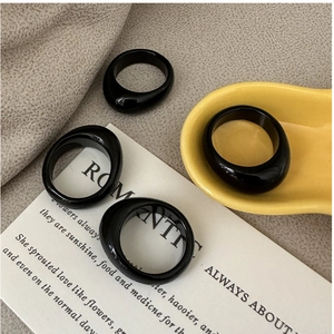Set of four minimalist glossy black resin rings displayed on a ceramic tray in a soft setting