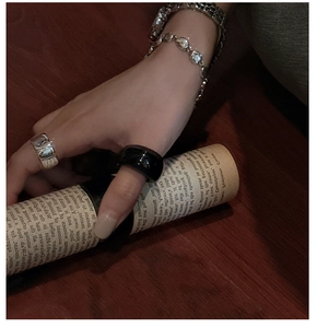 Minimalist silver and black rings with metallic chain bracelets on dark wood