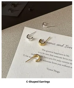 Detailed view of C-shaped layered silver and gold earrings on textured vintage paper