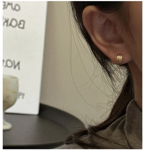 Detail of a gold triple-layer textured stud earring shown on an earlobe in a macro shot