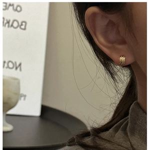 Close-up of a model wearing minimalist three-layer textured gold stud earrings
