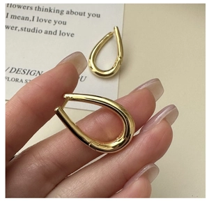 Close-up of golden teardrop earrings showing the S925 sterling silver hallmark engraving