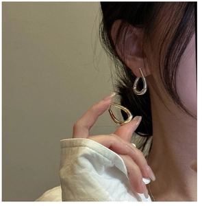 Polished silver and gold teardrop earrings shown on ear for minimalist style