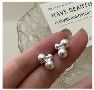 Close-up of matte S925 sterling silver triple ball stud earrings held by hand