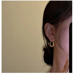 Close-up of minimalist gold twisted drop earrings worn on earlobe with a polished finish