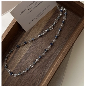 Gros plan du collier de perles en argent S925 avec cristaux bleus sur plateau en bois