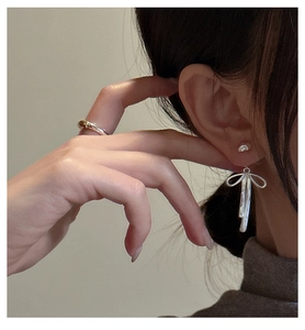Close-up of S925 sterling silver bow earrings and minimalist ring on a model