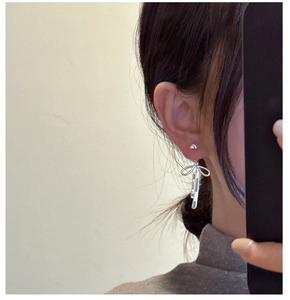 Detail of silver S925 bow earrings with dangling tassels shown worn on ear