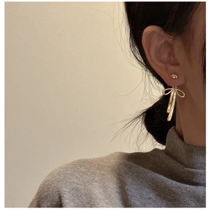 Close-up of elegant gold ribbon earrings with tassel pendants on Asian model