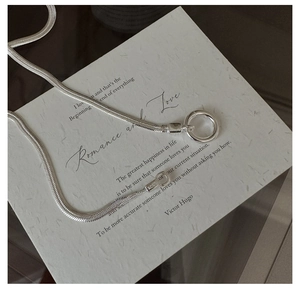 Detail of S925 sterling silver snake chain necklace with a round clasp on a textured card