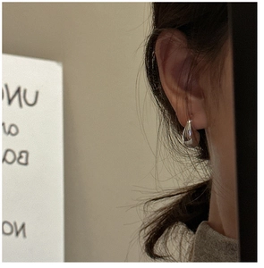 Close-up of polished silver teardrop earring worn by a model in a minimalist style