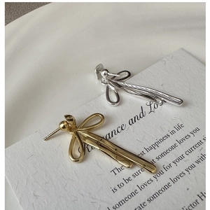 Detail of silver and gold textured bow dangle earrings on a minimalist display card