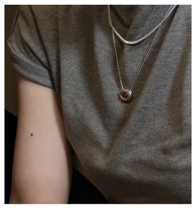 Detail of layered S925 silver snake chain and red gemstone pendant on a model