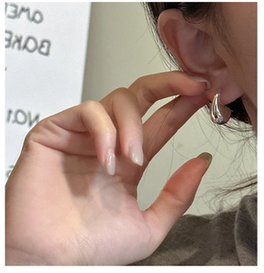 Close-up of polished silver teardrop earrings worn by a model in a minimalist style