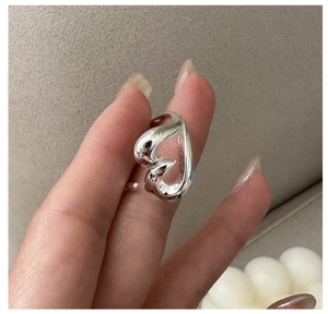 Close-up of liquid heart ring in silver finish held against a warm gray fabric background