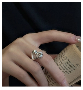 Detail of a large hollow heart-shaped silver ring on finger with vintage book background