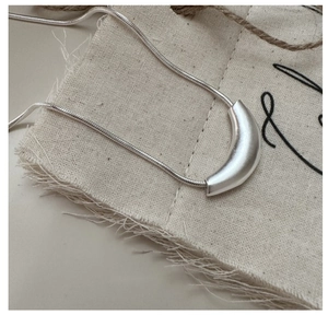 Macro shot of silver crescent pendant on snake chain over rustic linen fabric