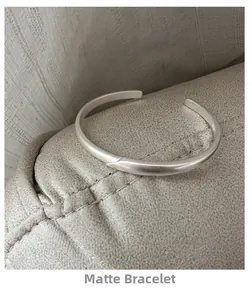 Macro shot of matte silver open cuff bracelet with overlapping layered design on gray fabric