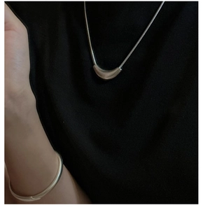 Close-up of minimalist S925 silver curved pendant necklace and sleek round bangle on model