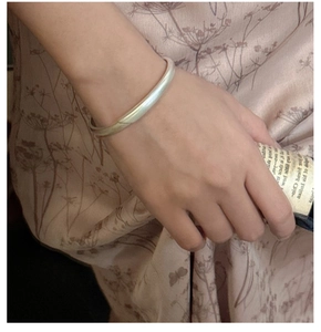 Macro detail of silver cuff bracelet with a matte finish worn on a floral dress background