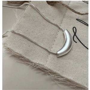 Macro shot of minimalist silver matte curved pendant necklace on a linen textile background
