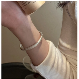Close-up of minimalist matte silver bangle worn with a cozy warm white knit sweater