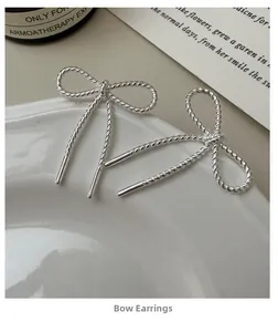 Detail of S925 silver bow earrings with twisted texture and long drop on a white plate