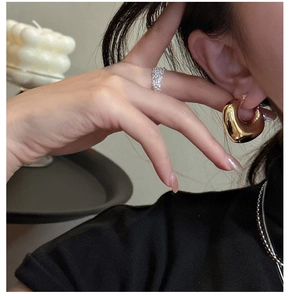 Detail shot of chunky gold C-shaped earrings and textured silver ring on a model
