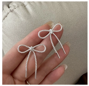 Detail of silver S925 bow earrings featuring a textured rope-like woven design and metallic finish