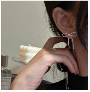 Detail of silver bow earrings with metal tassels worn by a model in a cozy setting