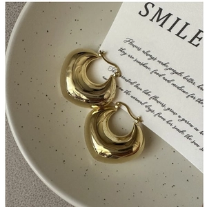 Detail of chunky gold drop earrings with mirror polish finish on a ceramic plate
