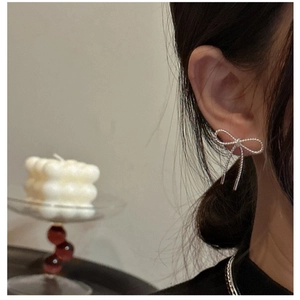 Detailed view of silver bow-shaped earring with twisted wire texture on model's ear