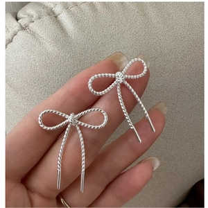 Macro detail of silver bow earrings with twisted rope texture and hanging linear metal bars