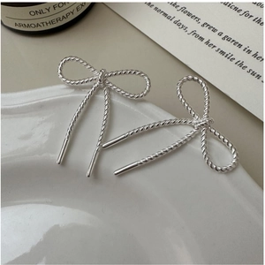 Close-up of S925 silver bow earrings with textured twist pattern on a ceramic tray