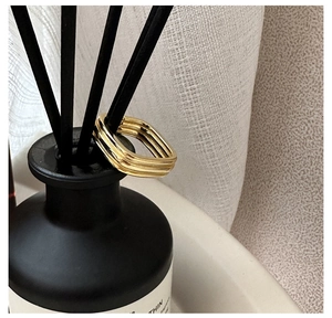 Close-up of triple-layered golden square ring with wavy texture on black diffuser sticks