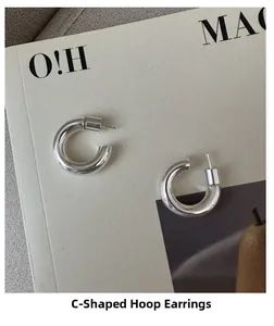 Macro shot of minimalist silver S925 C-shaped chunky hoop earrings on a magazine background