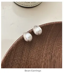 Close-up of S925 sterling silver bean stud earrings with a brushed metal texture