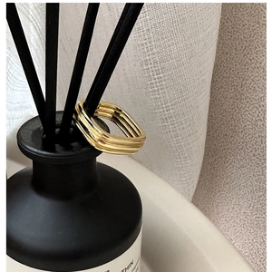 Detail view of a gold square multi-layered ring hanging on a black diffuser stick