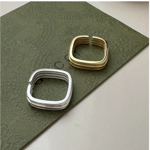 Detail of layered silver and gold square rings on a textured background