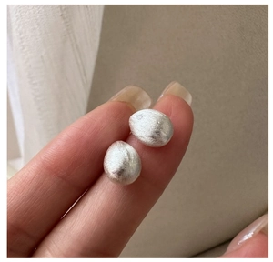Close-up of S925 sterling silver stud earrings with brushed metallic texture held by hand