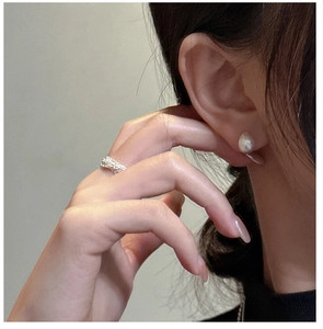 Macro shot of silver textured open ring and elegant white pearl stud earring on model