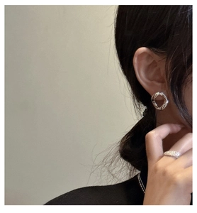 Gros plan sur un modèle portant des créoles torsadées en argent et une bague pailletée