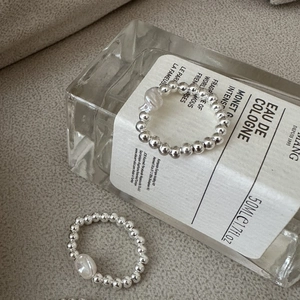 Detail of two handmade S925 silver beaded rings with irregular baroque pearls on a glass bottle