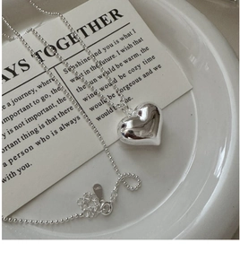 Detailed view of 3D hollow heart pendant and S925 silver beaded chain on a white plate