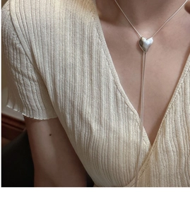 Dettaglio di una collana con ciondolo a cuore in argento e catena snake su una modella
